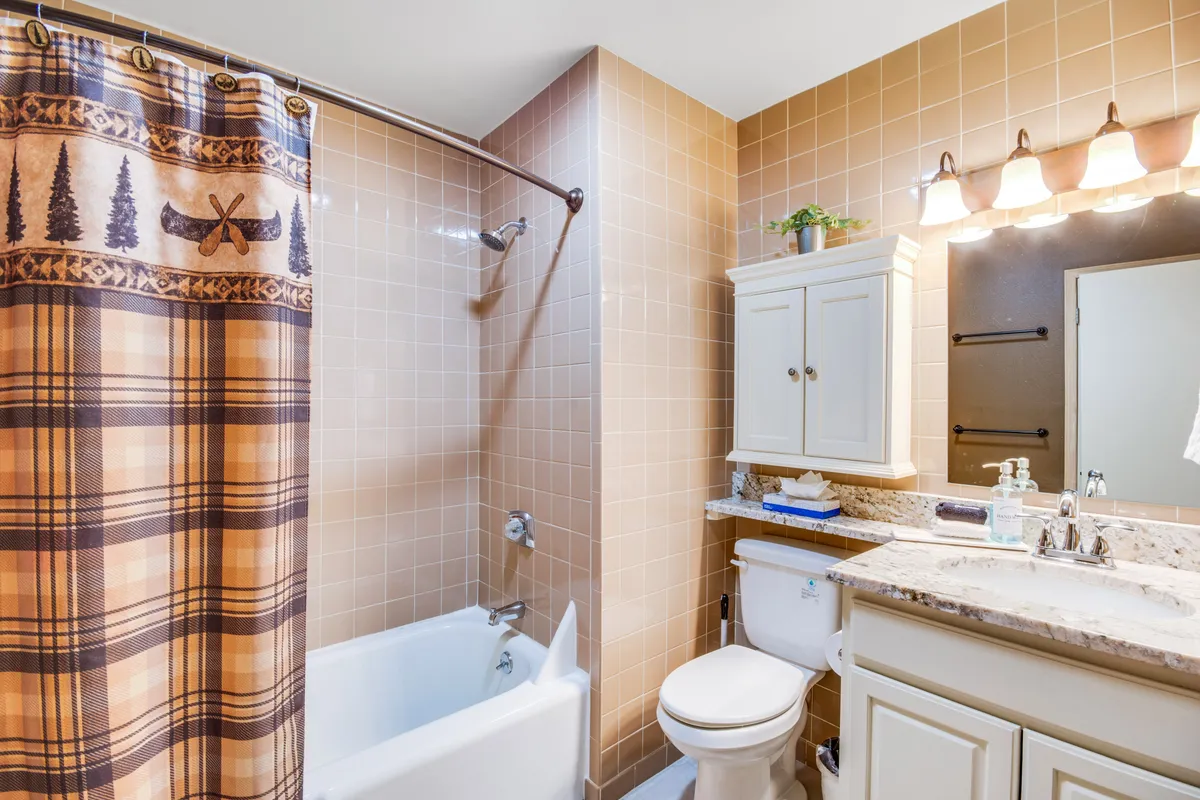 A welcoming bathroom with a granite countertop vanity, plaid and canoe-themed shower curtain, and soft lighting. Details like towels and decorative accents create a peaceful, functional space for personal routines.
