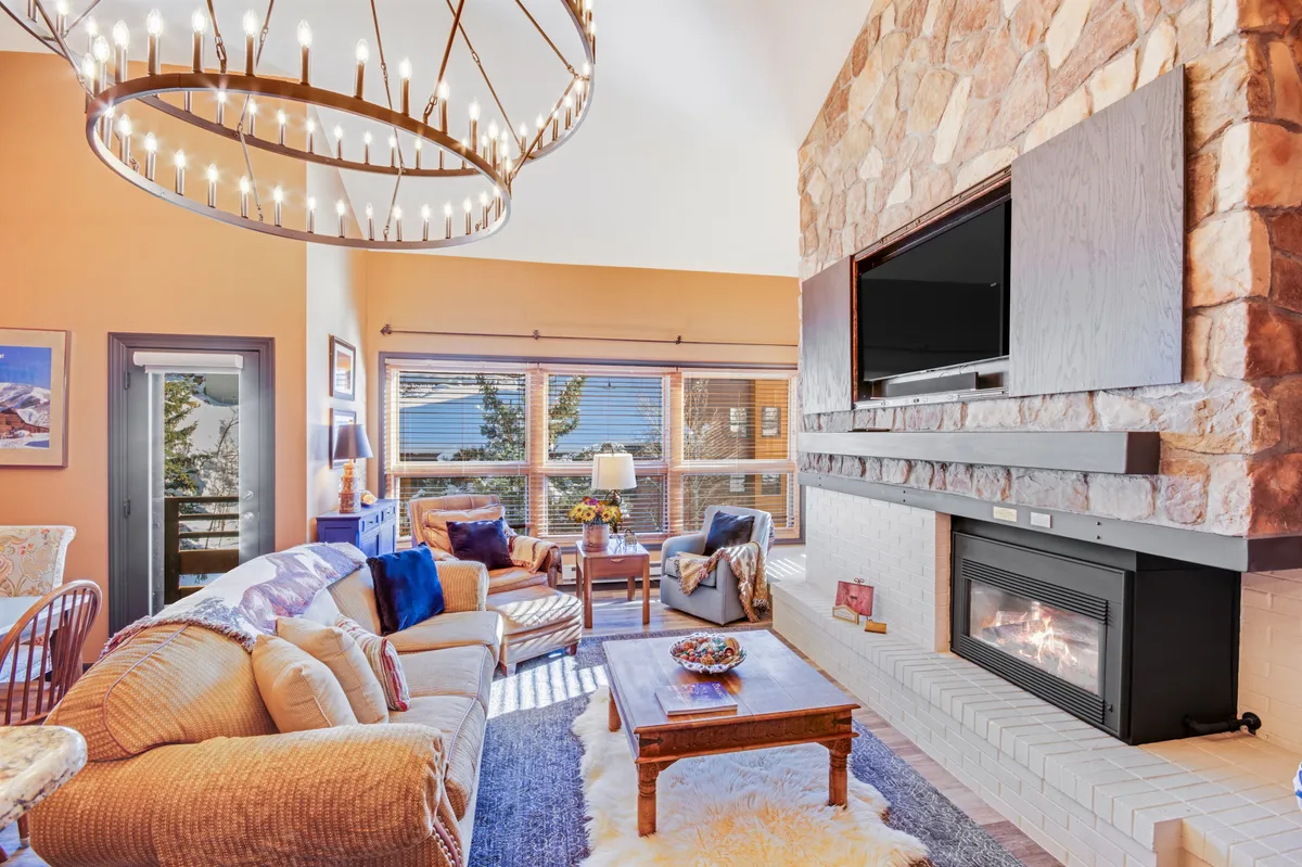 A comfortable living area anchored by a striking stone fireplace, plush sofas, and a gleaming chandelier overhead. The room's ambiance is both elegant and cozy, perfect for relaxing family evenings or entertaining friends beside a warm fire.