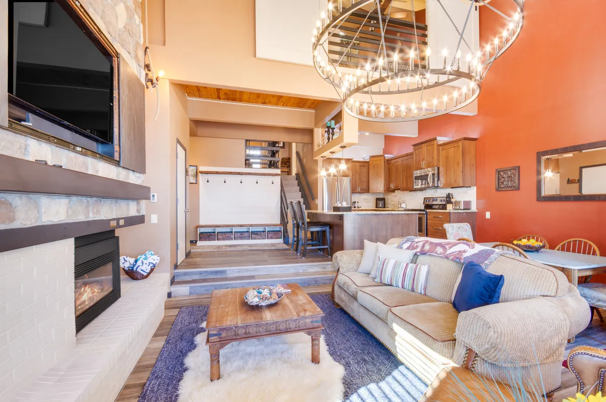 A spacious, open-concept living area with a cozy sofa, prominent fireplace, kitchen, and wooden dining table, offering a glimpse into the home’s social spaces ideal for entertaining and unwinding.