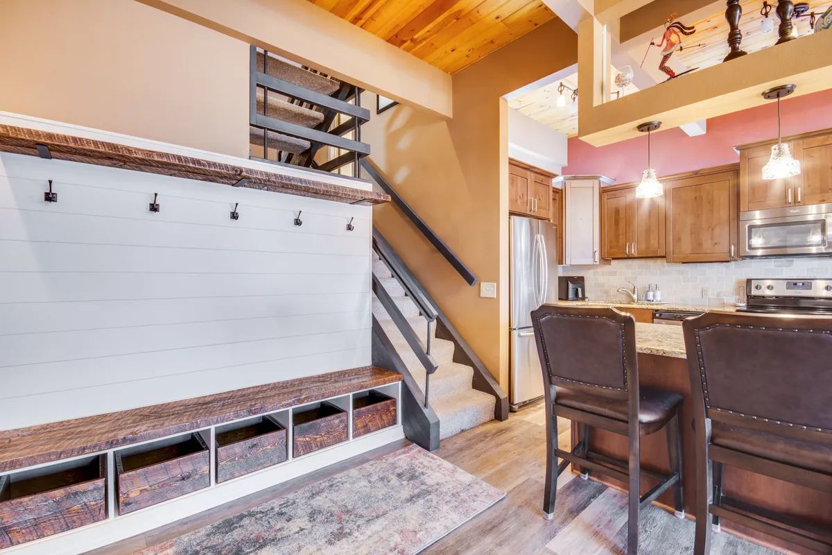 An interior shot focusing on a functional entry area with a bench and hooks for outdoor gear, leading into the kitchen. The space is cozy and organized, perfectly suited for storing ski equipment or getting ready for outdoor adventures.