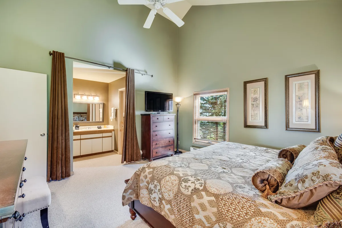 A spacious bedroom featuring a plush king bed adorned with decorative bedding, a wooden dresser, and a window allowing natural light to fill the room. The tranquil atmosphere is enhanced by soft colors and cozy furnishings, perfect for unwinding after a day outdoors.