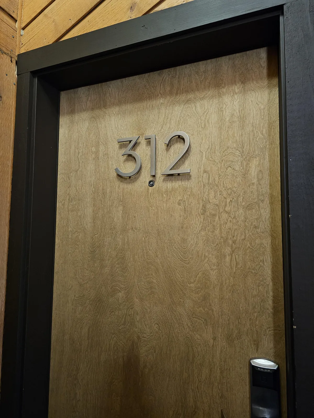 A close-up of the entrance door to Kutuk unit 312, featuring a wood-grain texture and clear door number, giving a welcoming first impression and emphasizing arrival and proximity to the action.