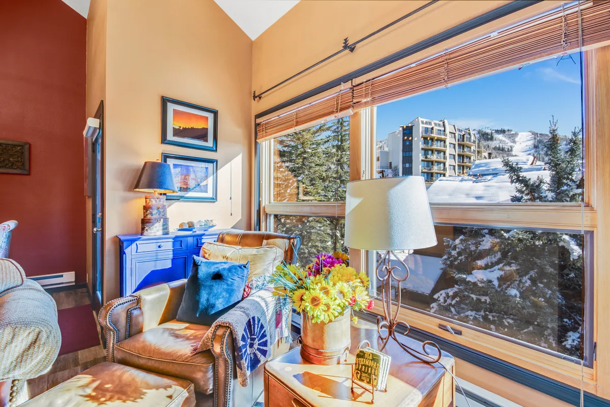 A cozy corner with leather armchairs, colorful pillows, a vibrant arrangement of flowers, and large windows that provide breathtaking mountain views. The atmosphere is warm and welcoming, ideal for reading, relaxing, or enjoying the landscape.